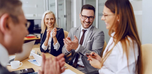 A group of business individuals clapping enthusiastically in a meeting setting, reflecting a positive atmosphere.